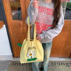 Detalle del bolso tote de lona amarilla con cierre de cordón y bordado de margarita