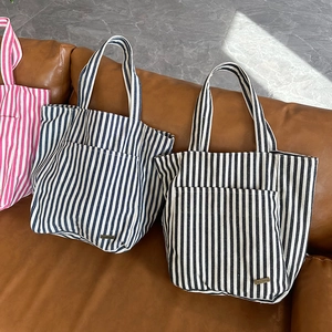 Dettaglio di grandi borse tote in tela a righe con tasche frontali in tre colori