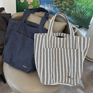 Dettagli di borse tote in denim blu e a righe con tasche frontali e logo in metallo