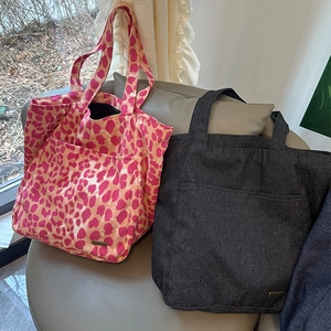 Dettaglio di borse tote in tela leopardata con doppie tasche frontali e targhette in metallo