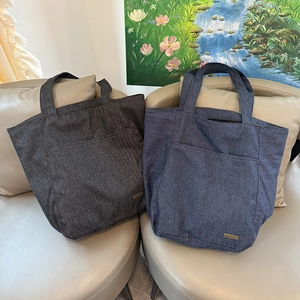 Dettaglio di borse tote in denim con tasche frontali e targhette logo in metallo