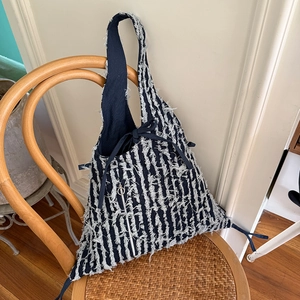 Gestreifte Denim-Tasche mit Fransen-Details und Quasten-Reißverschluss auf Vintage-Stuhl
