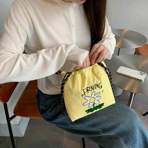 Detalle de bolso de nailon amarillo con bordado de margaritas y correa trenzada bicolor