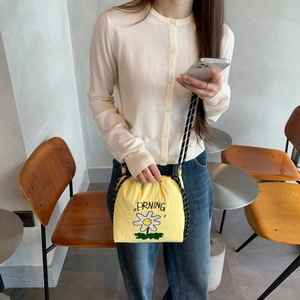 Detalle de bolso de nailon amarillo con bordado de margarita y correa trenzada