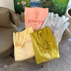 Détail de sacs cabas en toile imprimés grocery en quatre couleurs pastel sur un canapé