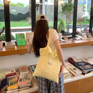 Close-up of light yellow ruffled tote bag with textured fabric in a cozy library setting