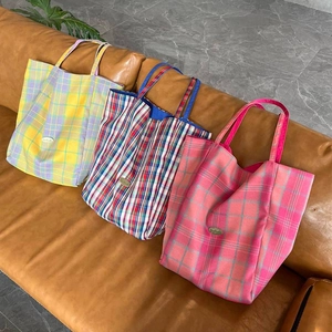 Three oversized plaid canvas tote bags in yellow, red, and pink on a leather sofa