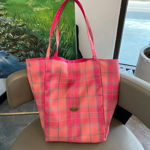 Detail of pink and orange checkered canvas tote bag with metal logo on a leather chair
