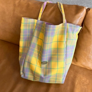 Detail of checkered canvas tote bag with retro metal buckle on a brown leather sofa