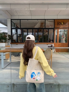 Detailed view of a beige canvas tote bag with cartoon bunny print and casual outfit