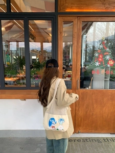 Detail of canvas mesh tote bag featuring cute cartoon illustrations on model's shoulder