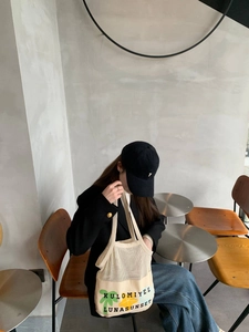 Detail view of cream mesh tote bag with green leaf print in a cafe setting
