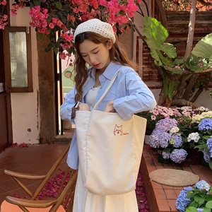 Outdoor shot of cream canvas tote bag with embroidered cat and wide shoulder strap