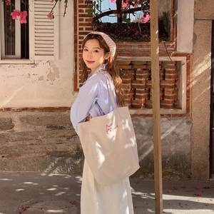 Minimalist beige canvas tote bag featuring an embroidered red cat and HELLO lettering