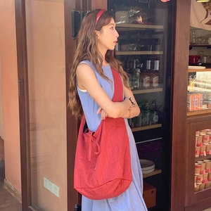 Detail of red oversized denim crossbody bag with textured pleats and wide shoulder strap