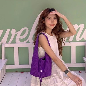 Detail view of purple pleated shoulder bag with texture on model in white dress