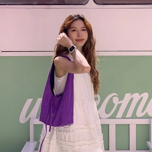 Close-up of purple striped fabric shoulder bag worn with a white dress in a bright setting