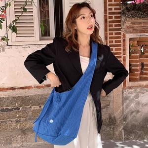 Close-up of blue vertical pleated denim crossbody bag showing fabric texture and badge