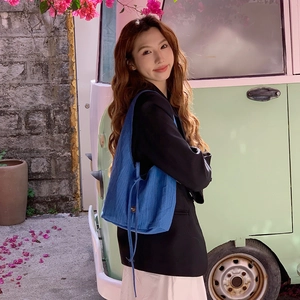 Blue denim tote bag with vertical texture and side tie detail worn by a model