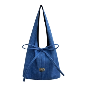 Blue denim tote bag with vertical stripes, central bow, and heart metal charm on white background