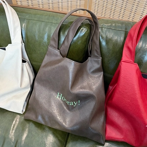 Close-up of three colorful PU leather tote bags with Hooray text on a leather sofa