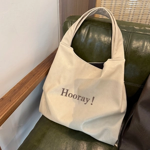 Detail of soft cream faux leather tote bag with brown Hooray lettering on green sofa