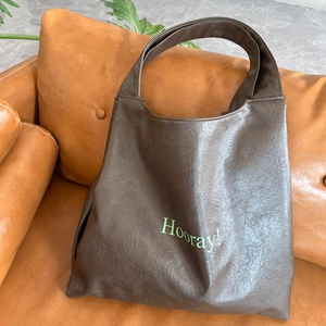 Detail of soft leather tote bag in dark coffee with green Hooray text on sofa