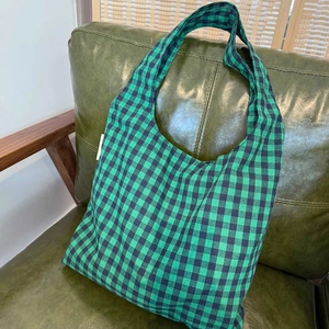 Detail of green checkerboard canvas tote bag on a green leather sofa with wide handle