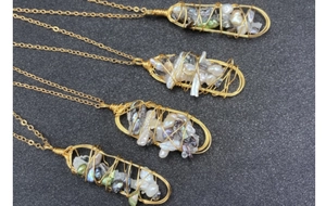 Dettaglio di ciondoli con perle barocche avvolti in fili dorati su catenine sottili
