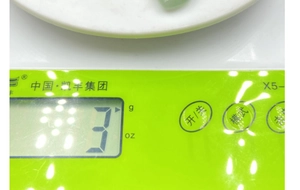 Vista macro di un ciondolo in giada verde chiaro del peso di 3g su una bilancia digitale