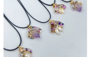 Close-up of handmade wire wrapped amethyst and pearl pendants on black cords