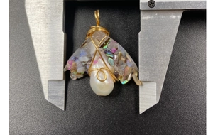 Macro view of handmade gold wire wrapped pearl pendant with iridescent shell inlay