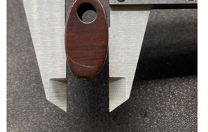 Measuring red agate pendant width with a metal caliper for handmade jewelry size check
