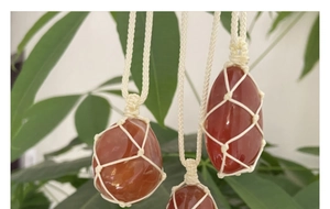 Detailed view of hand-woven net pouch necklaces with raw red agate stones on green leaves