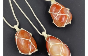 Detailed view of three handmade macrame necklaces with raw red agate stones on black background
