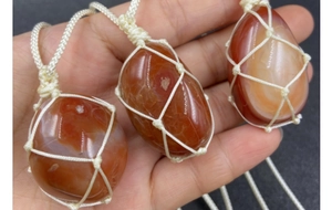 Close-up of three polished natural carnelian stones in handmade woven mesh pouches