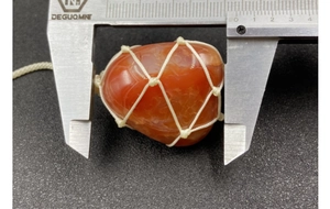 Macro shot of red agate stone pendant in net bag measured by silver caliper for size