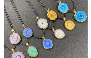 Macro shot of colorful geode crystal slice pendants with gold plated edges and black cords