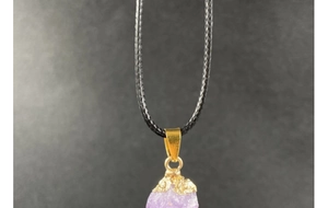 Macro shot of natural purple amethyst raw gemstone pendant with golden clasp and black cord