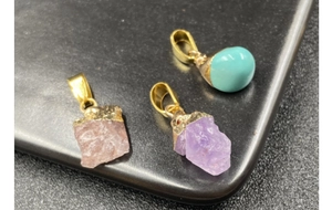 Close-up of raw amethyst, rose quartz, and turquoise pendants with golden metal clasps