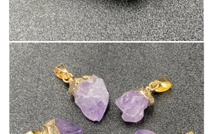 Macro shot of natural raw amethyst stone pendants with gold metal clips on dark fabric