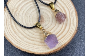 Detail of amethyst and strawberry quartz raw stone pendants on a rustic wood slice