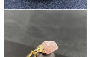 Close-up of raw rose quartz stone pendant with gold clasp on textured background