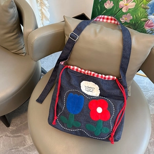 Detail of blue denim tote bag with red tulip embroidery and checkered drawstring closure