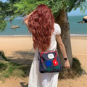 Detail of dark blue denim tote with floral embroidery and red drawstring on a sunny beach
