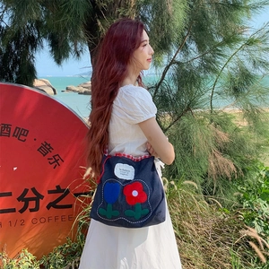 Detailed view of floral embroidery on navy denim tote bag with red gingham drawstring closure
