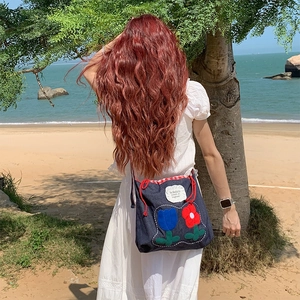 Detail of navy denim drawstring bag with tulip embroidery on scenic beach background