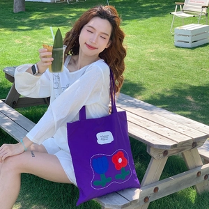 Detail of purple canvas tote with tulip embroidery in a sunny outdoor garden setting