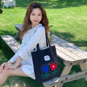 Detailed embroidery of colorful flowers and white text on a black canvas tote bag