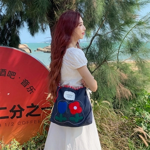 Denim tote bag with tulip embroidery and red checkered trim in a bright outdoor setting